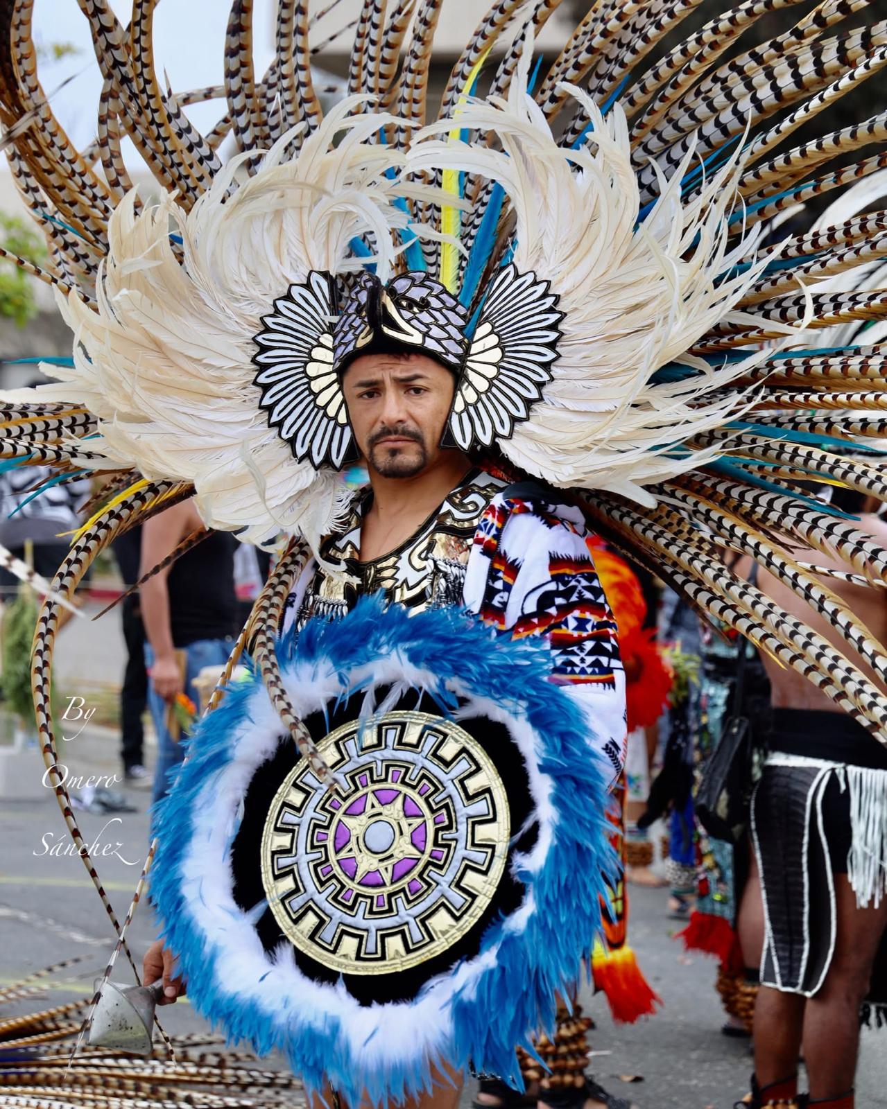 Aztec warrior with large white feathered headdress and blue feathered shield